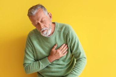 Olgun bir adam sarı arka planda kalp krizi geçiriyor.