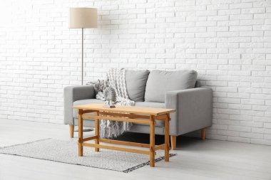 Beyaz tuğla duvarın yanında kanepesi ve lambası olan açık ahşap bir sehpa.