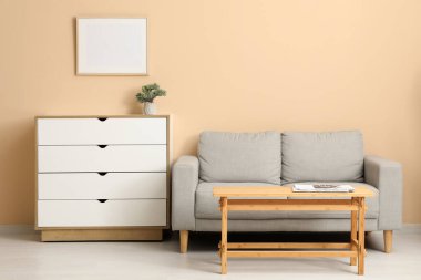 Bej duvarın yanında kanepesi ve şifoniyeri olan açık ahşap sehpa.