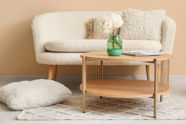 Tahta sehpa, kanepe ve bej duvarın yanında yastıklar.