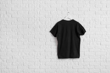 Beyaz tuğla duvarda asılı şık siyah tişört