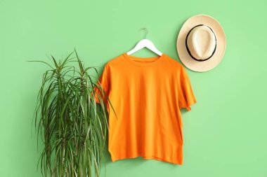 Yeşil arka planda asılı şık turuncu tişört ve şapka