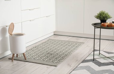 Modern mutfağın içinde şık halı, çöp kutusu ve beyaz tezgahlar var.