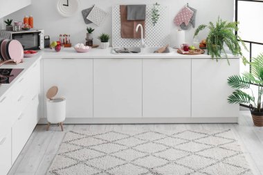 Modern mutfağın içinde şık halı, çöp kutusu ve beyaz tezgahlar var.