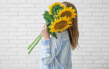 Hafif tuğlalı arka planda güzel ayçiçekleri olan kadın.