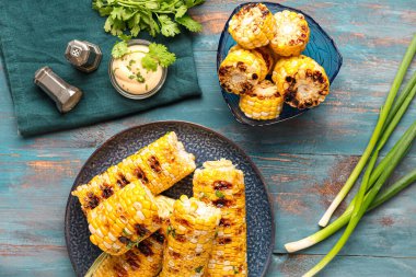 Mavi ahşap arka planda maydanozlu bir tabak dolusu lezzetli mısır koçanı.