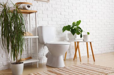 Seramik klozet, raf ünitesi ve beyaz tuğla duvarın yanındaki evlerin olduğu açık tuvaletin içi.