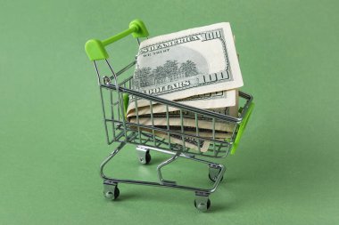 Yeşil arka planda dolar banknotları olan alışveriş arabası, yakın plan.