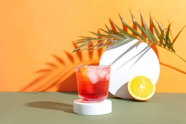 Bir bardak soğuk Negroni kokteyli, arkaplanda portakal ve palmiye yaprağı.