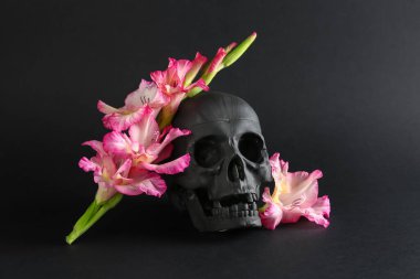 Siyah arka planda güzel zambak çiçekleri olan insan kafatası