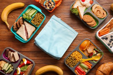 Çanta, farklı lezzetli yemekler ve kahverengi ahşap arka planda meyveler.