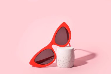 Pembe arka planda şık güneş gözlüklü dekoratif podyum