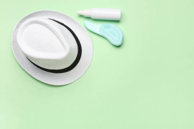 Şık şapka, saç fırçası ve arka planda bir şişe güneş kremi.