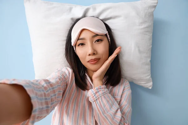 青い背景にセルフィーを取る枕を持つパジャマで美しいアジアの女性 — ストック写真