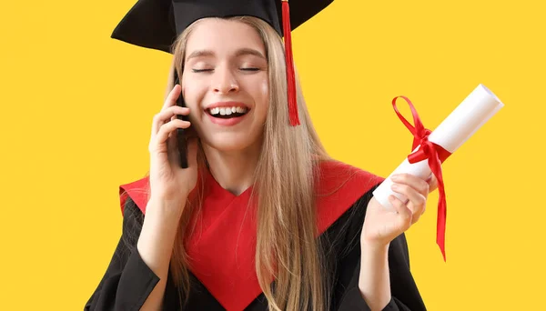 黄色い背景で携帯電話で話す卒業証書を持つ女性の大学院生 — ストック写真