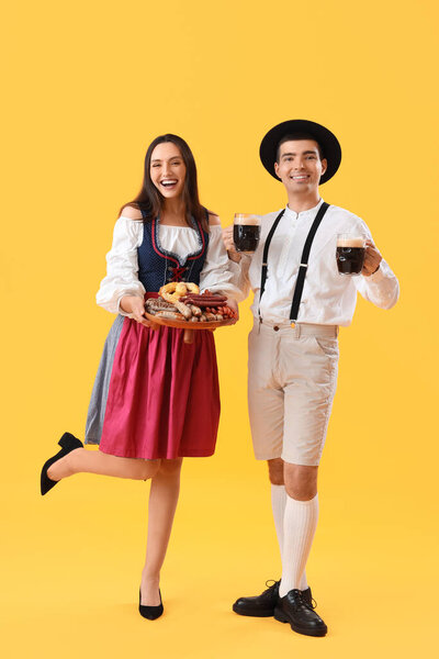 Молодая пара в традиционной немецкой одежде с пивом и закусками на желтом фоне