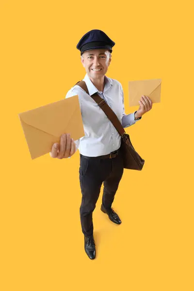 成熟したポストマンと黄色の背景の封筒 — ストック写真