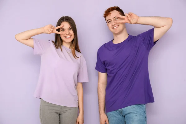 Młoda Para Shirtach Pokazująca Gest Zwycięstwa Liliowym Tle — Zdjęcie stockowe