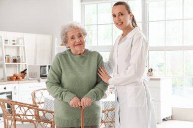 Elinde baston olan yaşlı bir kadın ve mutfakta kadın bir doktor.