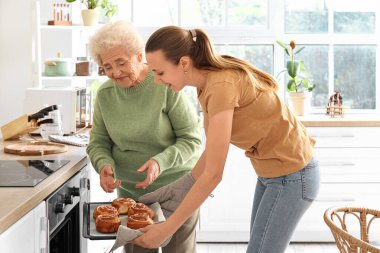 Torunuyla kıdemli bir kadın mutfakta fırından çörek alıyor.