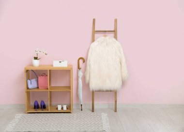 Salondaki pembe duvarın yanında paltosu olan raf, şemsiye ve merdiven.