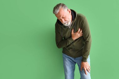 Olgun bir adam yeşil arka planda kalp krizi geçiriyor.