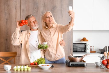 Domatesli olgun bir çift mutfakta selfie çekiyor.