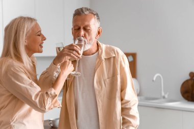 Olgun bir çift mutfakta şampanya içiyor.