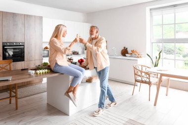 Olgun bir çift mutfakta şampanya içiyor.