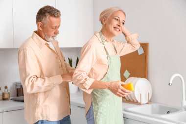 Olgun bir adam mutfakta karısına önlük bağlıyor.