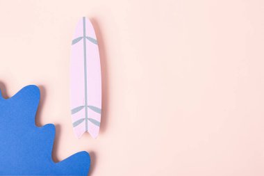 Kağıt dalgaları ve pembe arka planda mini sörf tahtası olan yaratıcı kompozisyon