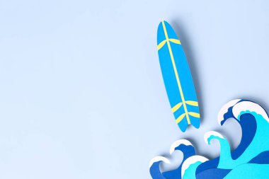 Mavi zemin üzerinde kağıt dalgaları ve mini sörf tahtası olan yaratıcı kompozisyon