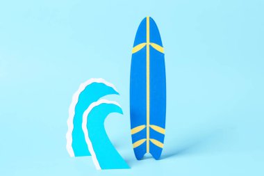 Mavi zemin üzerinde kağıt dalgaları ve mini sörf tahtası olan yaratıcı kompozisyon