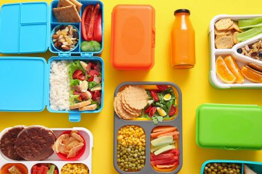 Farklı lezzetli yemekleri ve sarı arka planda bir şişe meyve suyu olan bir sürü beslenme çantası.