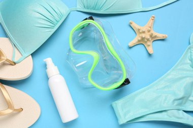 Yüzme maskesi, terlik, mayo ve mavi arka planda bir şişe güneş kremi.