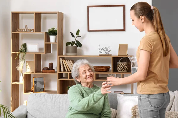 Yaşlı kadın evde torunundan bir bardak su alıyor.