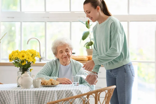 Young Woman Pouring Water Glass Her Grandmother Kitchen — Stock Photo, Image