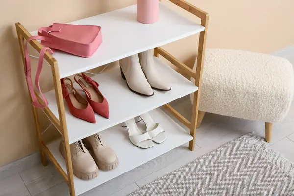 Koridordaki bej duvarın yanındaki raflarda ayakkabı ve bank var. Yakın çekim.