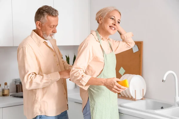 Mature man tying apron on his wife in kitchen