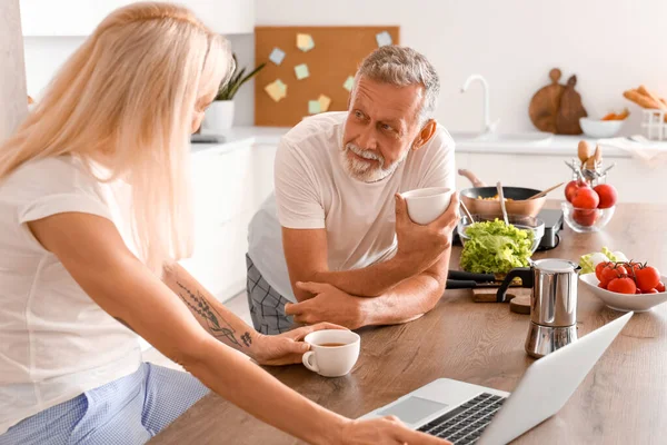 Mature couple with laptop drinking coffee in kitchen