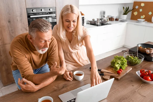 Mature couple with laptop watching video in kitchen