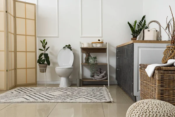 İçinde seramik klozet, raf ünitesi ve ev bitkileri olan ışık tuvaleti.