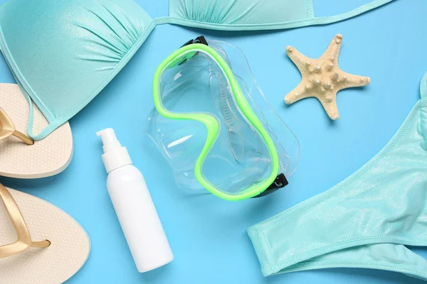 Yüzme maskesi, terlik, mayo ve mavi arka planda bir şişe güneş kremi.