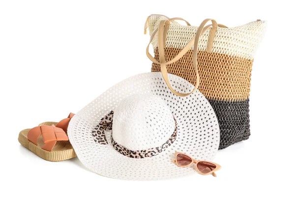 Beyaz arka planda şık bir plaj şapkası, çanta, terlik ve güneş gözlüğü.