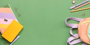 Okul çantası ve yeşil arkaplan üzerine farklı kırtasiye malzemesi.