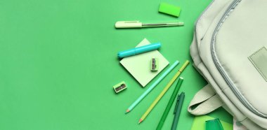 Okul çantası ve yeşil arkaplan üzerine farklı kırtasiye malzemesi.