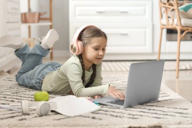 Kulaklıklı, dizüstü bilgisayarlı küçük bir kız evde bilgisayar bilimleri okuyor.