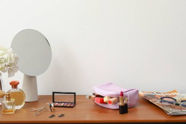 Farklı dekoratif kozmetik ürünleri ve ahşap masadaki ayna.