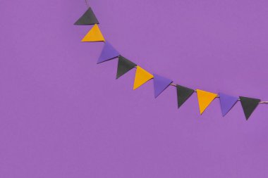 Cadılar Bayramı kutlamaları için mor arka planda kağıt bayraklardan yapılmış çelenkler.