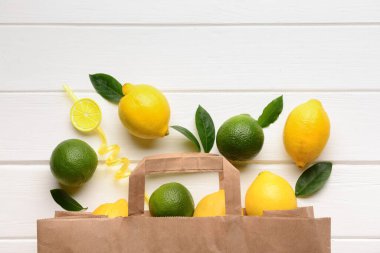 Beyaz ahşap arka planda taze limon ve limon dolu kağıt torba.